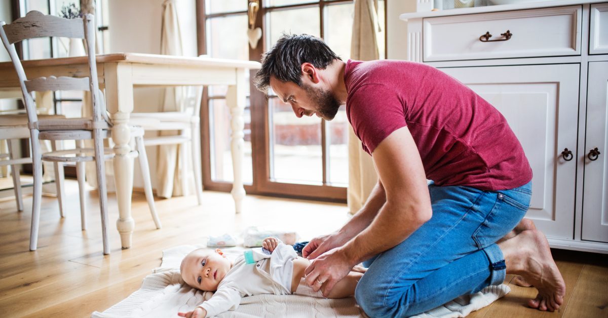 Father changing a baby girl at home. Paternity leave.