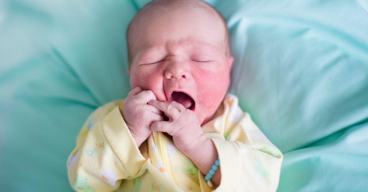 Newborn baby boy in bed. New born child sleeping on a green blanket. Children sleep. Bedding for kids. Infant napping in bed. Healthy little kid shortly after birth. Tired baby yawning.